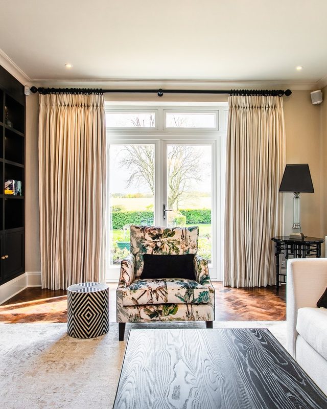 Montagu sitting room with long cream curtains, a patterned armchair and garden doors