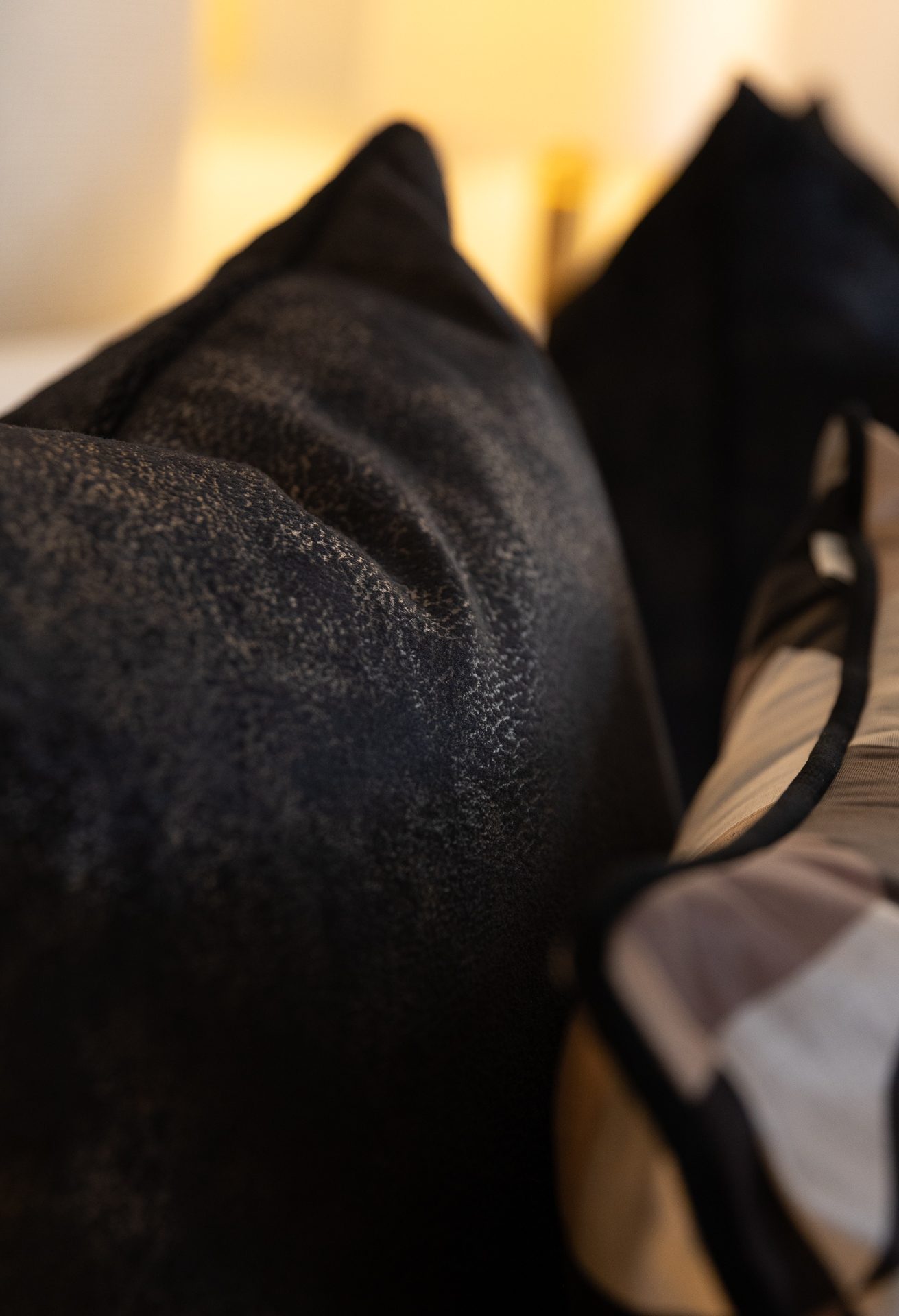 A close-up of a black antique-velvet cushion and a plain black cushion beside a warm lamp, header image for the Linen chapter