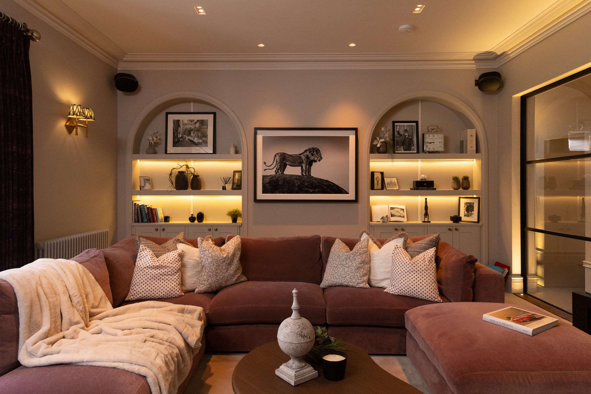 The snug, a deep plum sofa with arched niche shelving and warm accent lighting